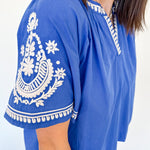 Blue top with white embroidery on a plain background