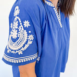 Blue top with white embroidery on a plain background