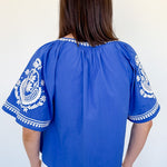 Woman wearing a blue blouse with white embroidery against a white background