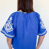 Woman wearing a blue blouse with white embroidery against a white background