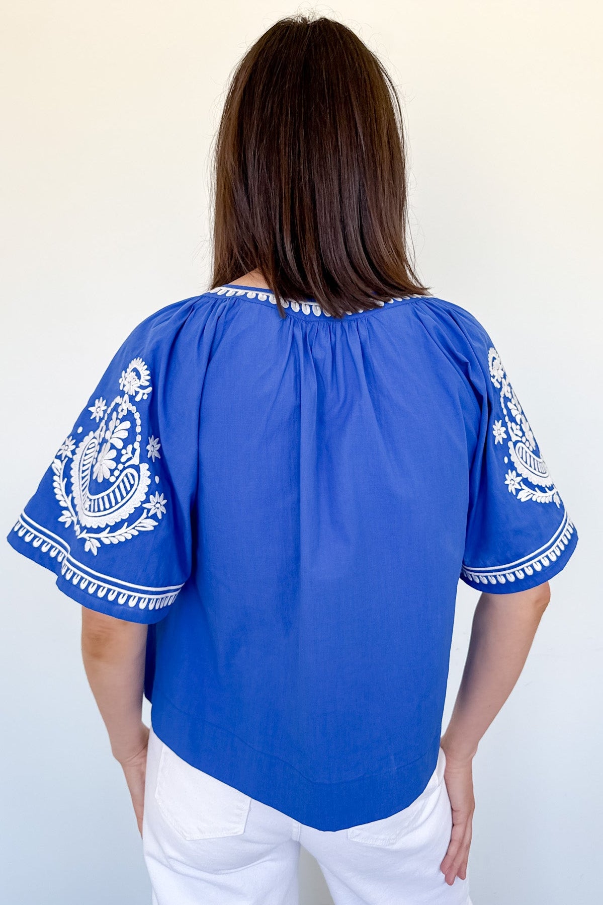 Woman wearing a blue blouse with white embroidery against a white background
