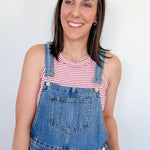 Woman wearing blue denim overalls and a red and white striped shirt against a plain background