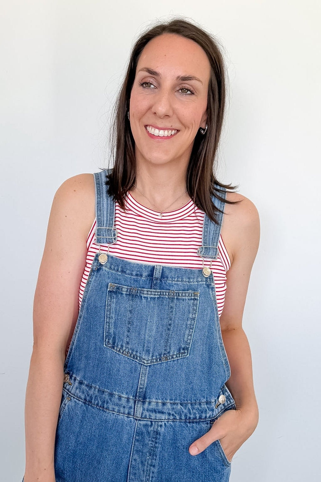 Woman wearing blue denim overalls and a red and white striped shirt against a plain background