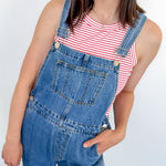 A woman wearing a red and white tank that is striped with blue overalls.