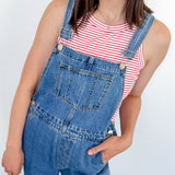 A woman wearing a red and white tank that is striped with blue overalls.