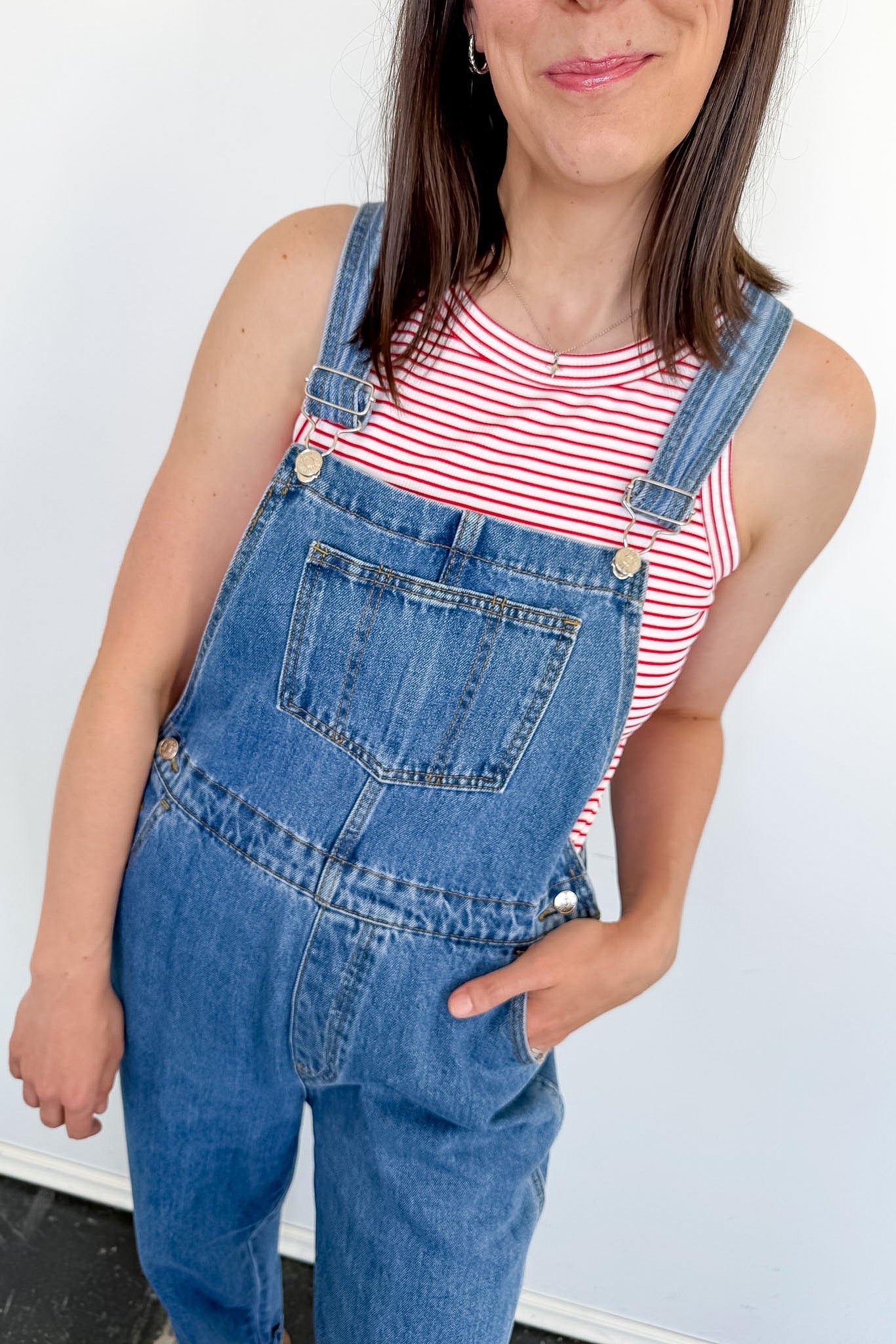 A woman wearing a red and white tank that is striped with blue overalls.