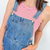 A woman wearing a red and white tank that is striped with blue overalls.