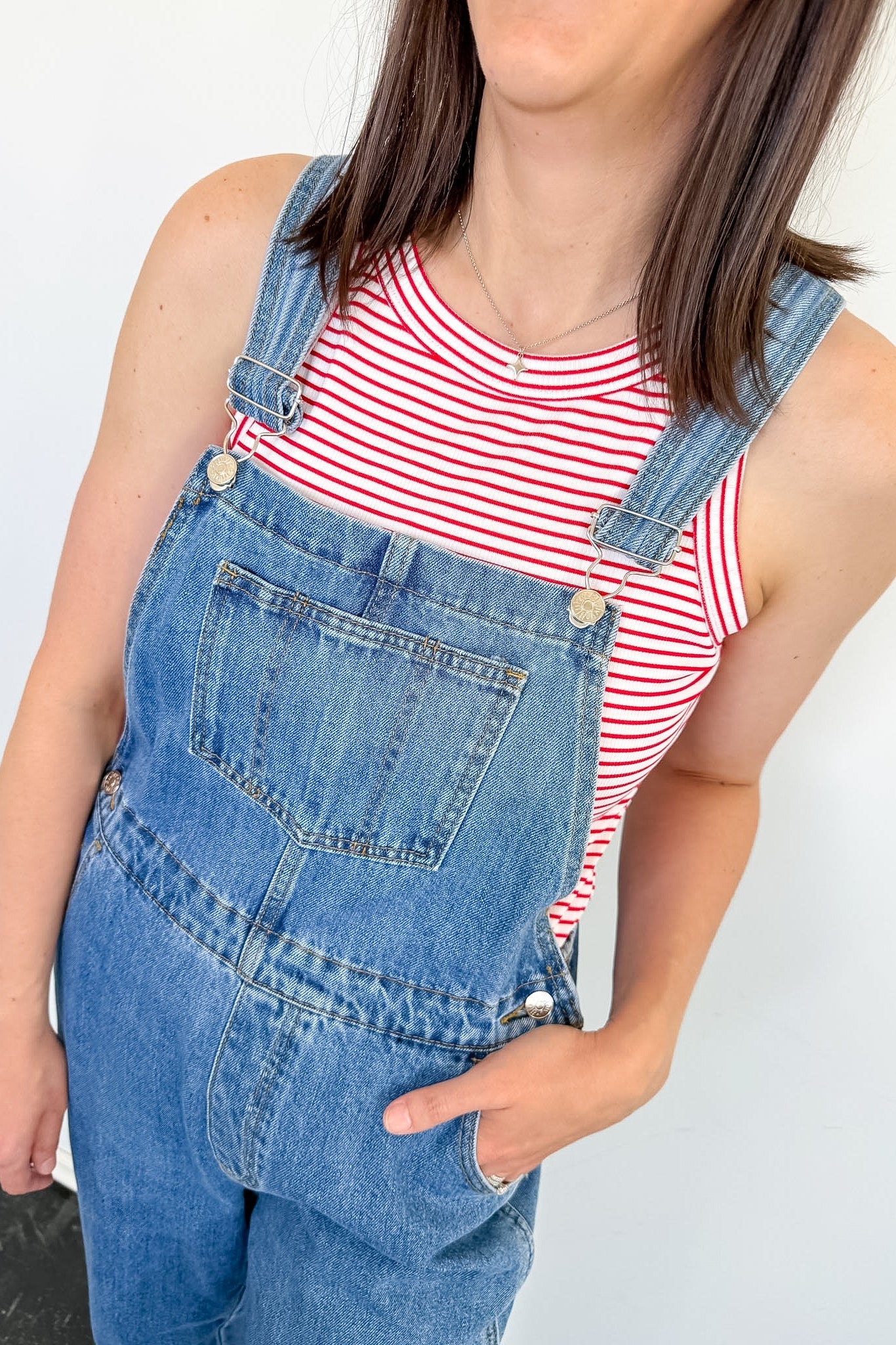 A woman wearing a red and white tank that is striped with blue overalls.