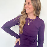 Woman wearing a purple long-sleeve top and blue jeans against a white background