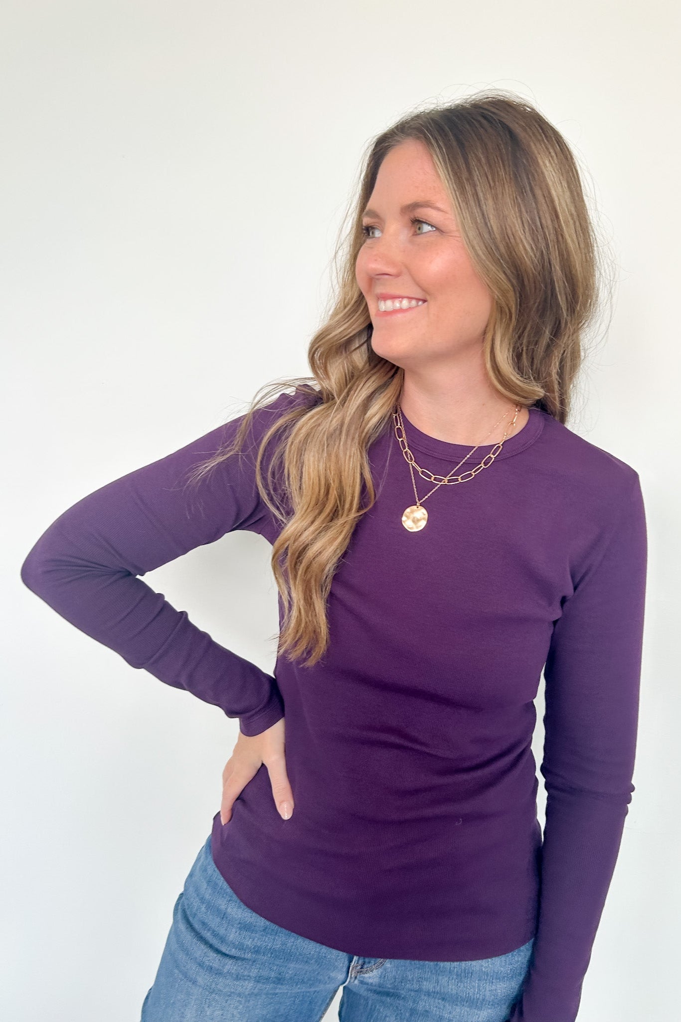 Woman wearing a purple long-sleeve top and blue jeans against a white background