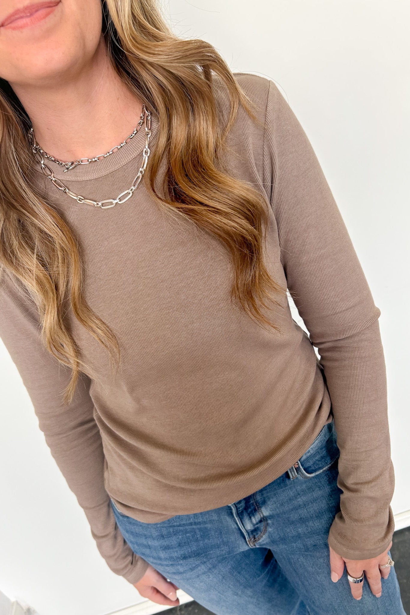 Person wearing a brown long-sleeve top and blue jeans on a white background