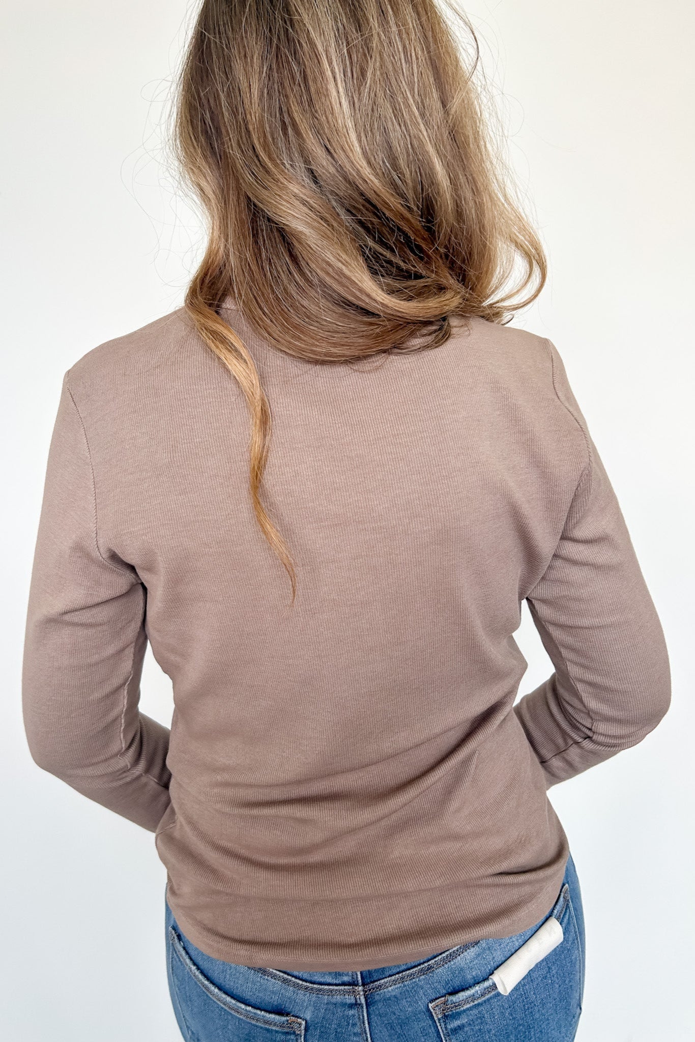 Person wearing a brown long-sleeve top and blue jeans on a white background