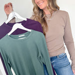 Woman holding two long-sleeve shirts, one green and one purple, against a white background.