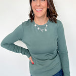 Woman wearing a green long-sleeve top and blue jeans against a white background
