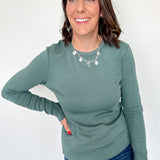 Woman wearing a green long-sleeve top and blue jeans against a white background
