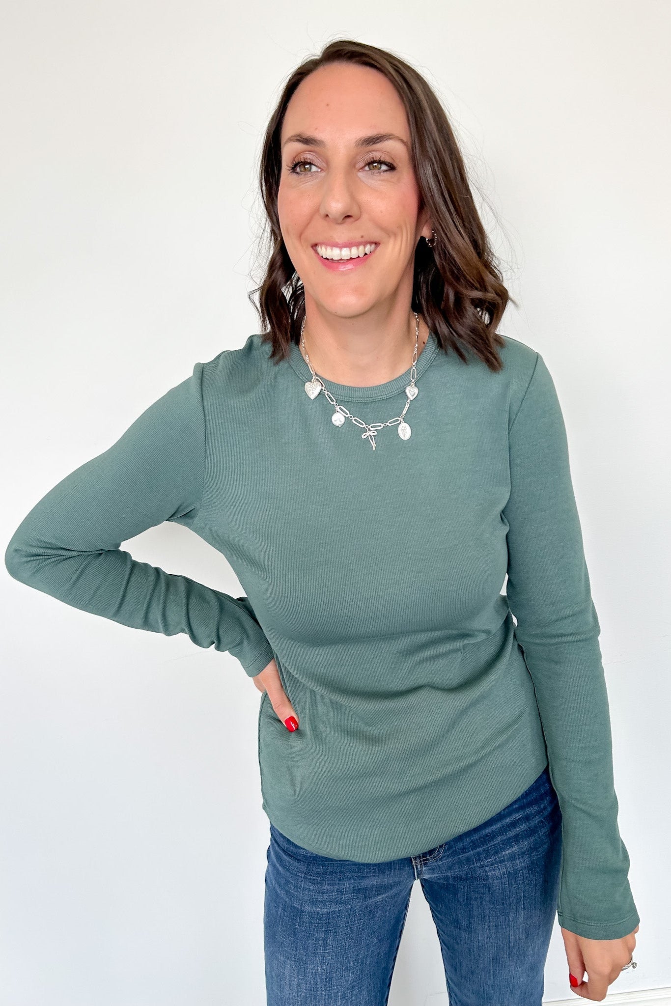 Woman wearing a green long-sleeve top and blue jeans against a white background