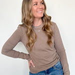 Woman wearing a brown long-sleeve top and blue jeans against a white background