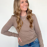 Woman wearing a brown long-sleeve top and blue jeans against a white background