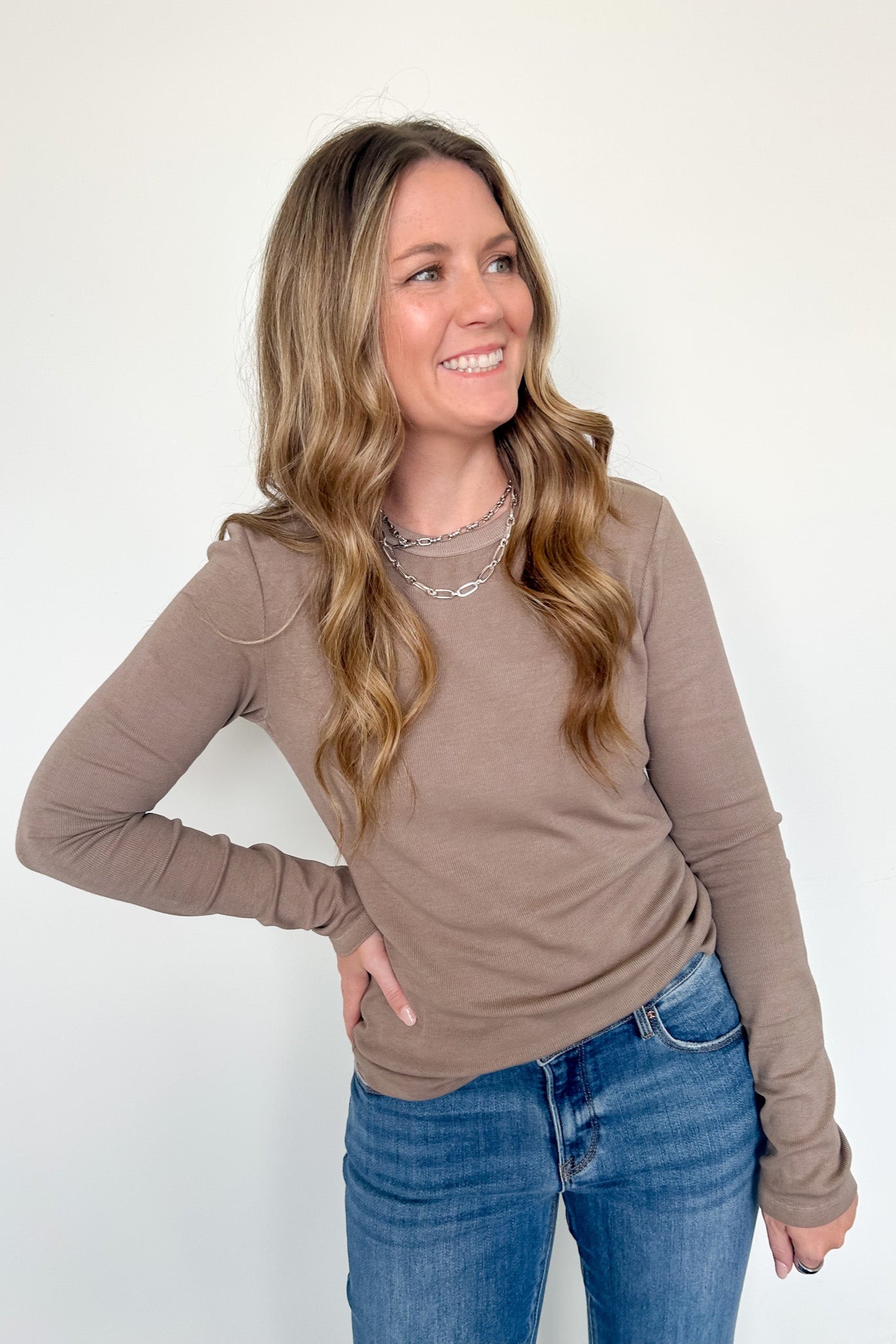 Woman wearing a brown long-sleeve top and blue jeans against a white background