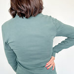 Person wearing a green long-sleeve top and blue jeans on a white background