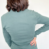 Person wearing a green long-sleeve top and blue jeans on a white background