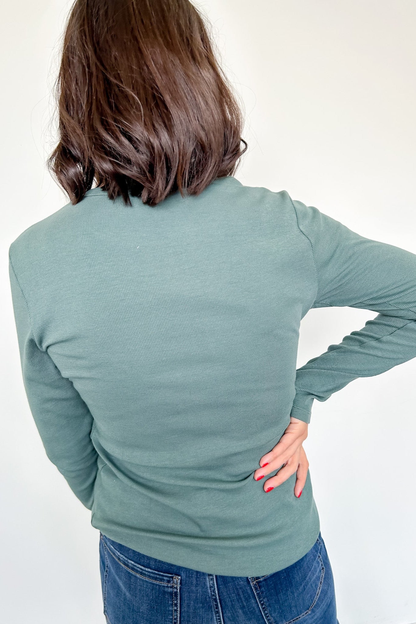 Person wearing a green long-sleeve top and blue jeans on a white background