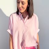 Woman wearing a pink short-sleeve blouse and pink pants against a gray background