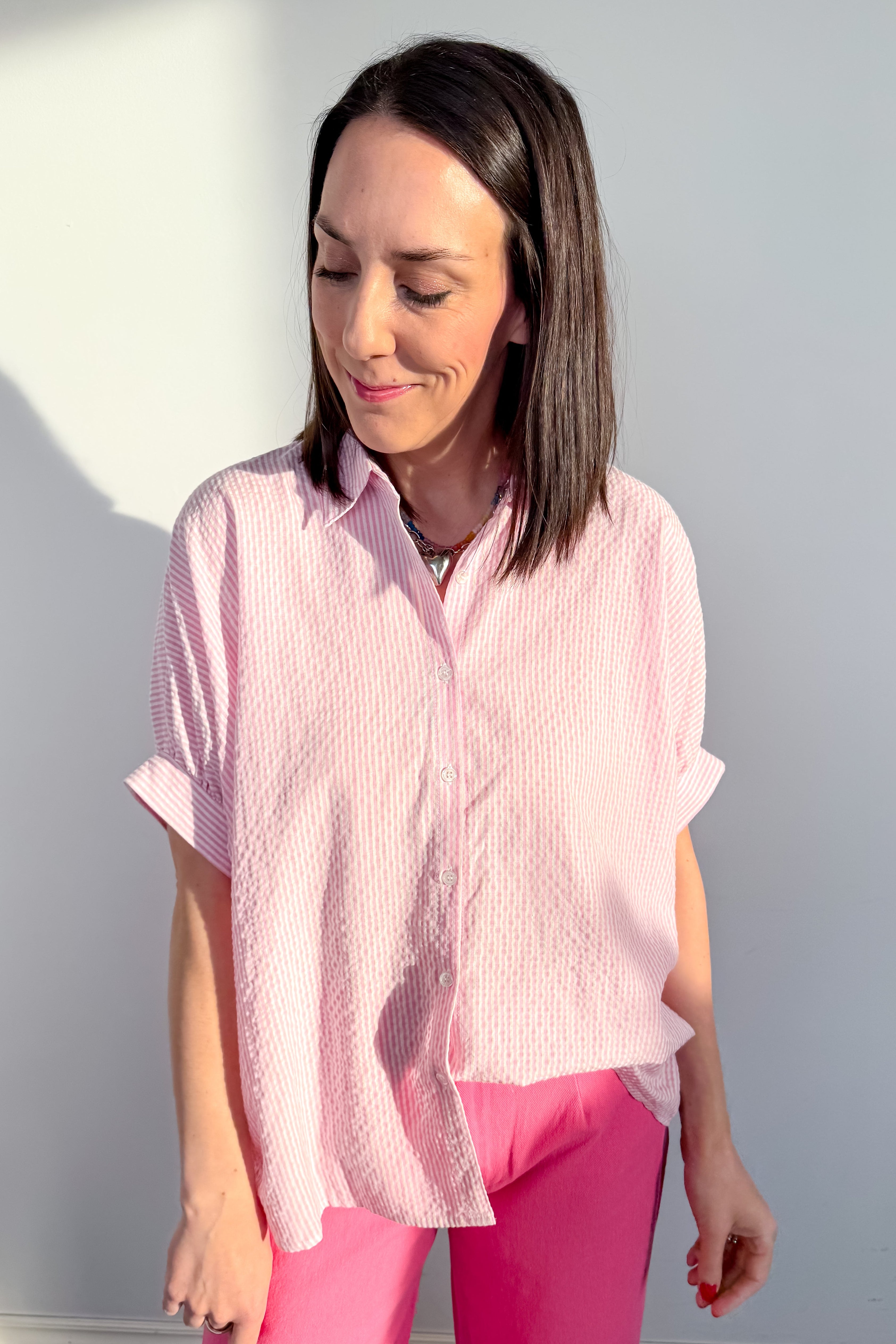 Woman wearing a pink short-sleeve blouse and pink pants against a gray background