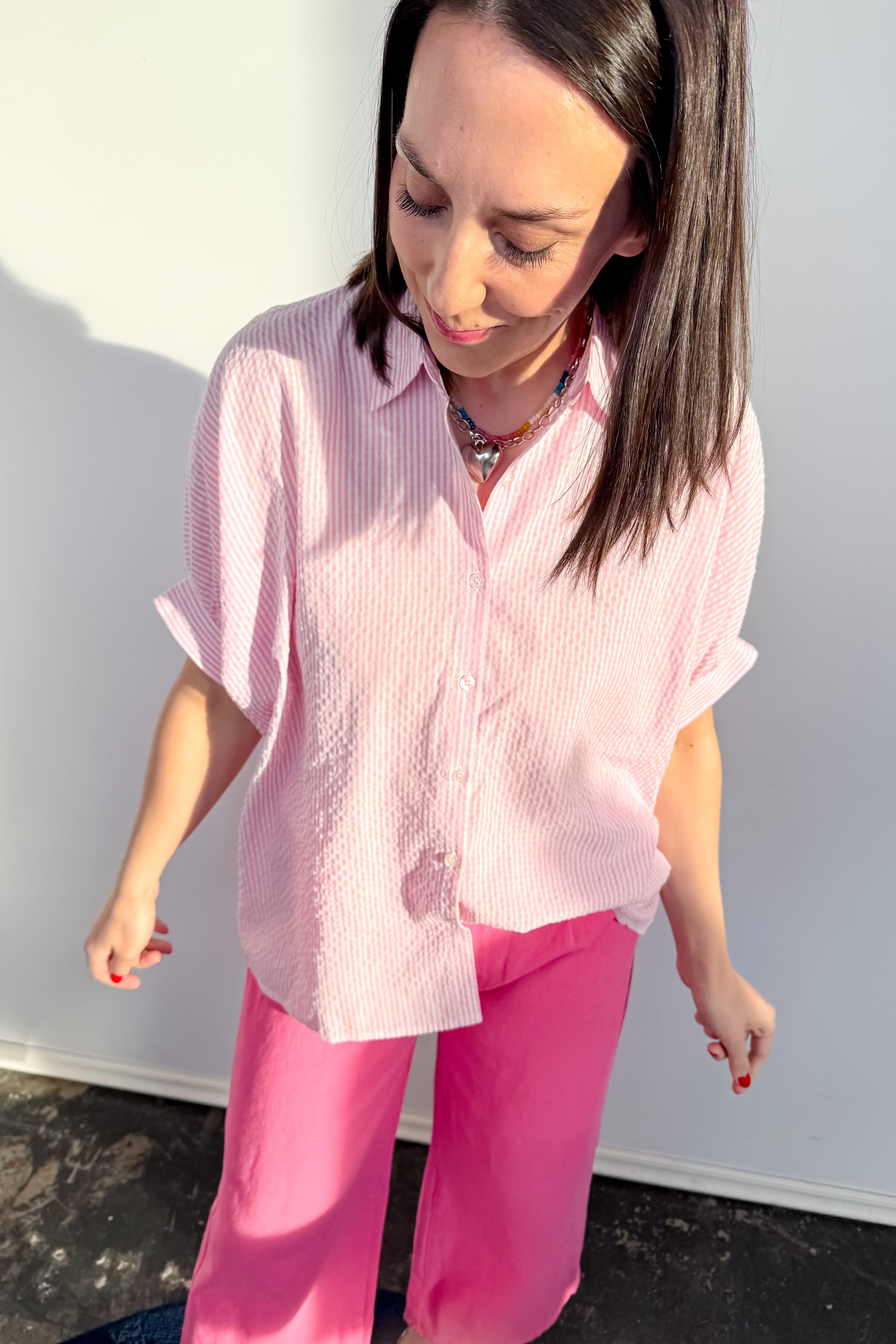 Woman wearing a pink striped shirt and pink pants against a white wall.