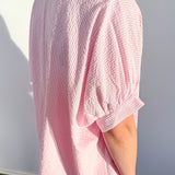 Person wearing a pink textured blouse against a white background