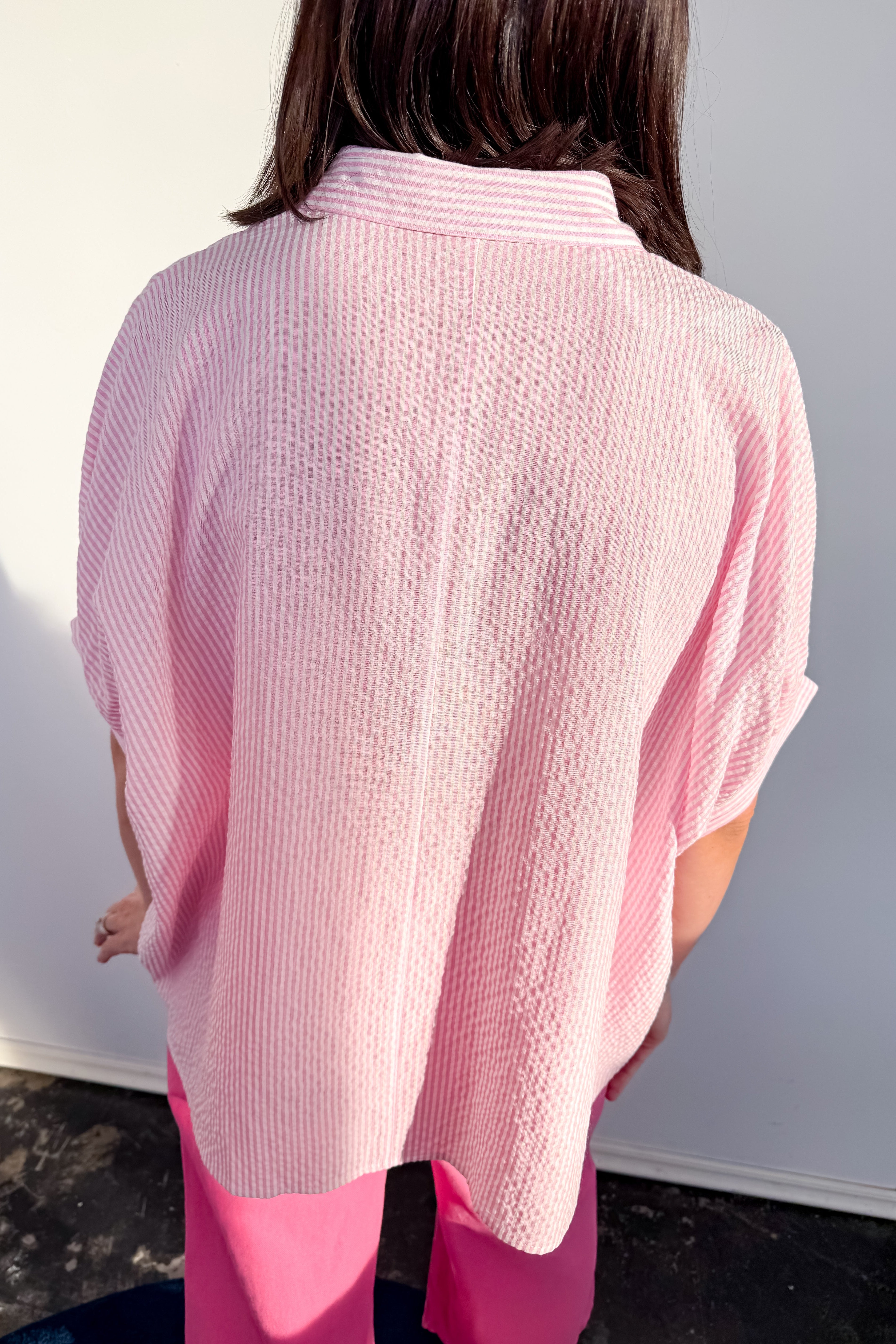 Person wearing a pink textured shirt against a white wall