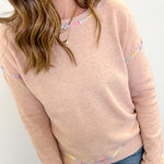 Woman wearing a light pink sweater with colorful accents on a white background