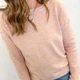 Woman wearing a light pink sweater with colorful accents on a white background