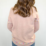 Person wearing a light pink sweater with colorful trim on a white background