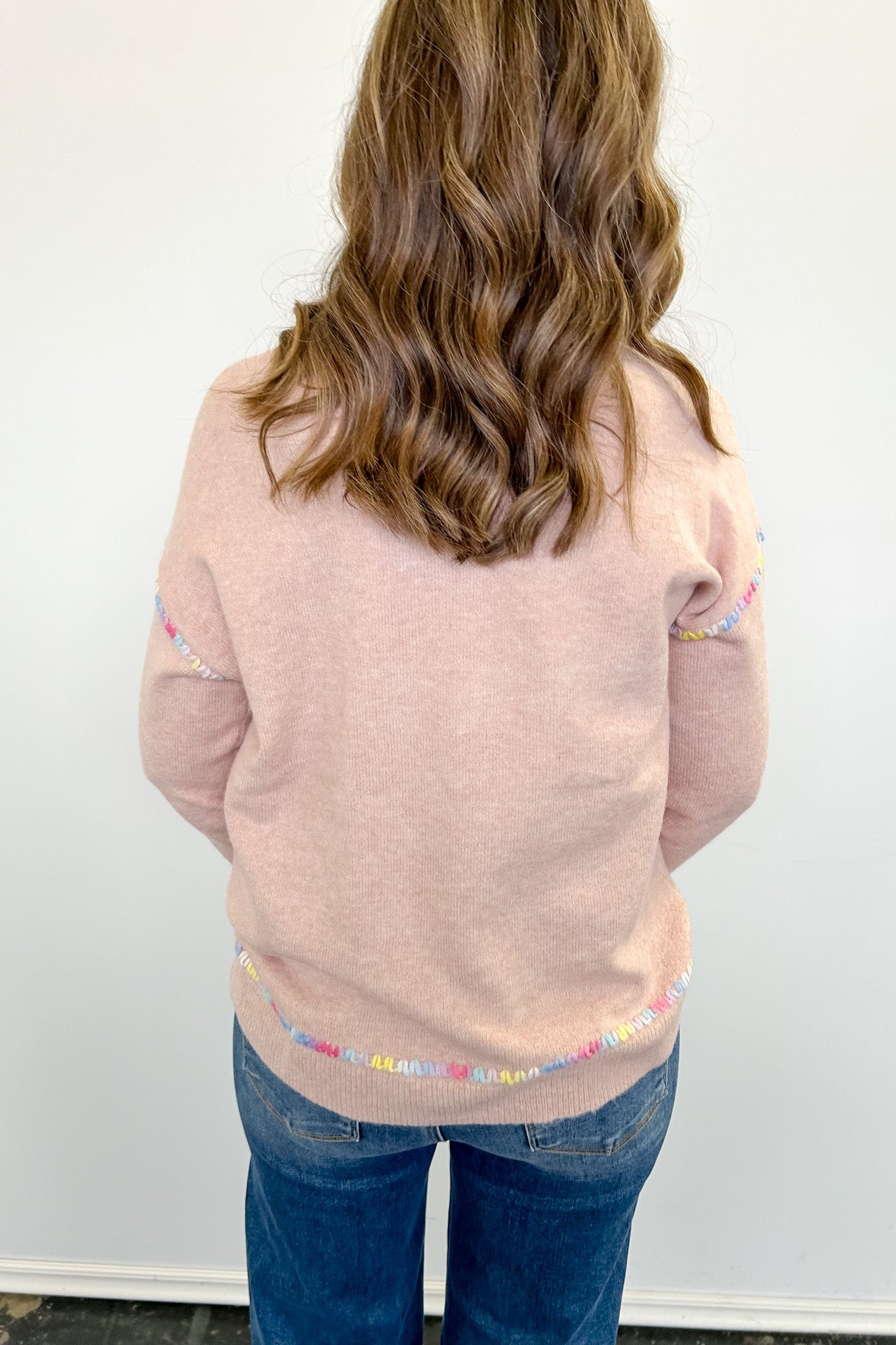 Person wearing a light pink sweater with colorful trim on a white background