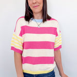 Woman wearing a striped sweater with pink, yellow, and white colors against a plain background