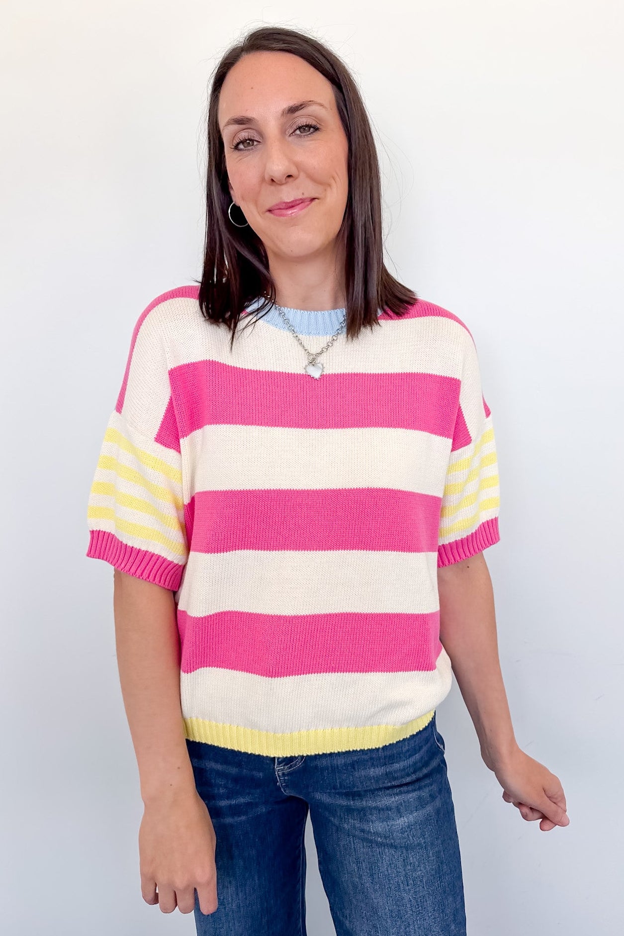 Woman wearing a striped sweater with pink, yellow, and white colors against a plain background