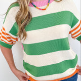 Person wearing a colorful striped sweater with green, orange, and white stripes on a plain background.