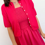 Woman wearing a bright pink dress with a matching cardigan against a white background