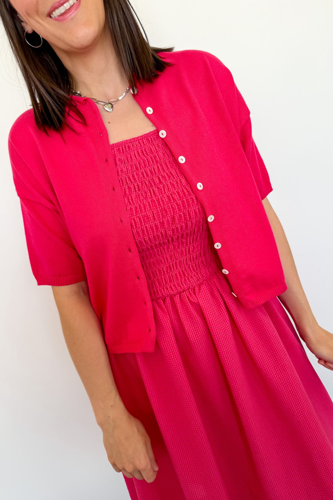 Woman wearing a bright pink dress with a matching cardigan against a white background