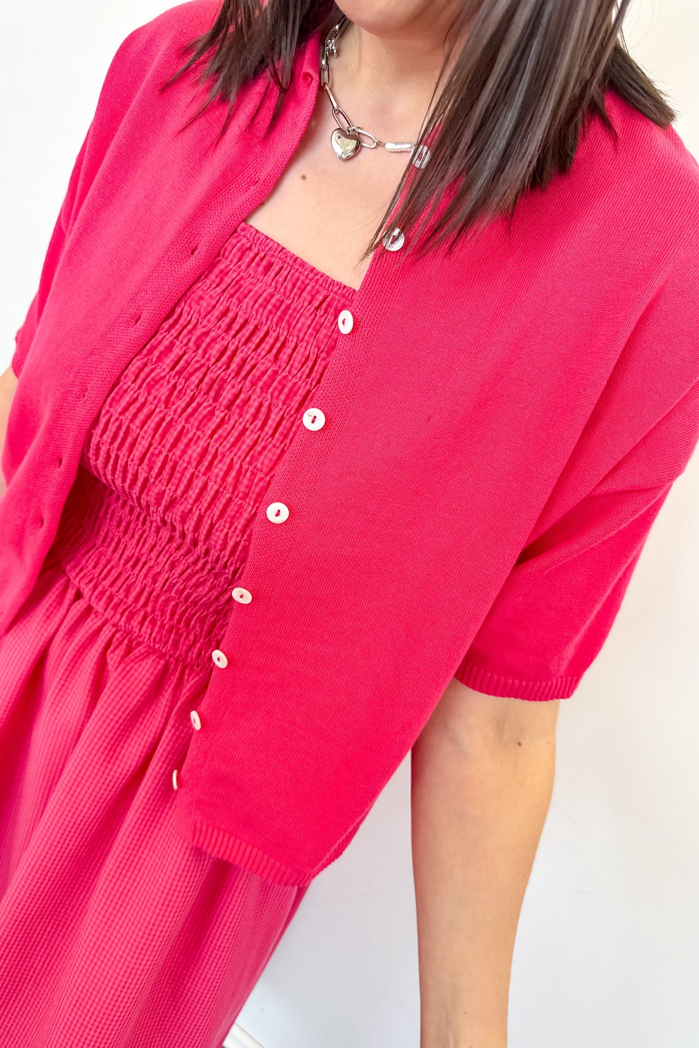Person wearing a bright pink dress with a matching cardigan on a white background