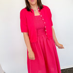 Woman wearing a bright pink dress and matching jacket indoors.