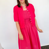 Woman wearing a bright pink dress and matching jacket indoors.