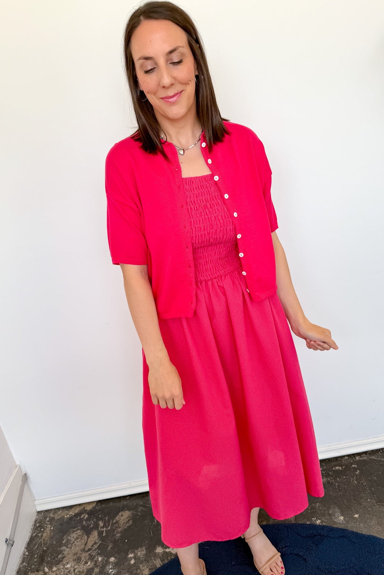 Woman wearing a bright pink dress and matching jacket indoors.