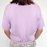 Person wearing a light purple sweater and patterned pants on a white background