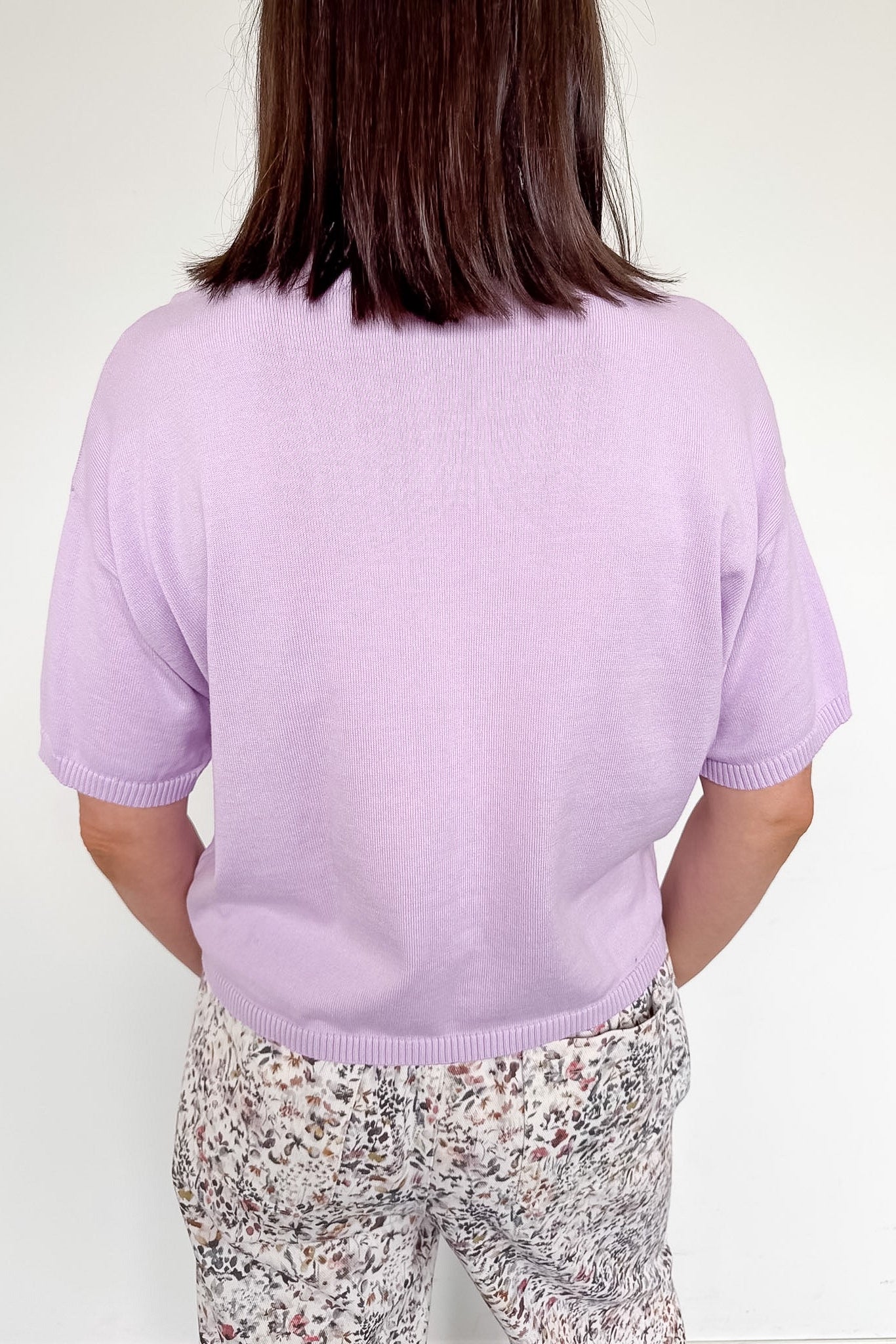 Person wearing a light purple sweater and patterned pants on a white background