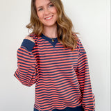 Woman wearing a red and navy striped sweater with blue jeans against a white background