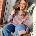 Woman sitting on a step outside, wearing a striped shirt and jeans.