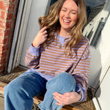 Woman sitting on a step outside, wearing a striped shirt and jeans.