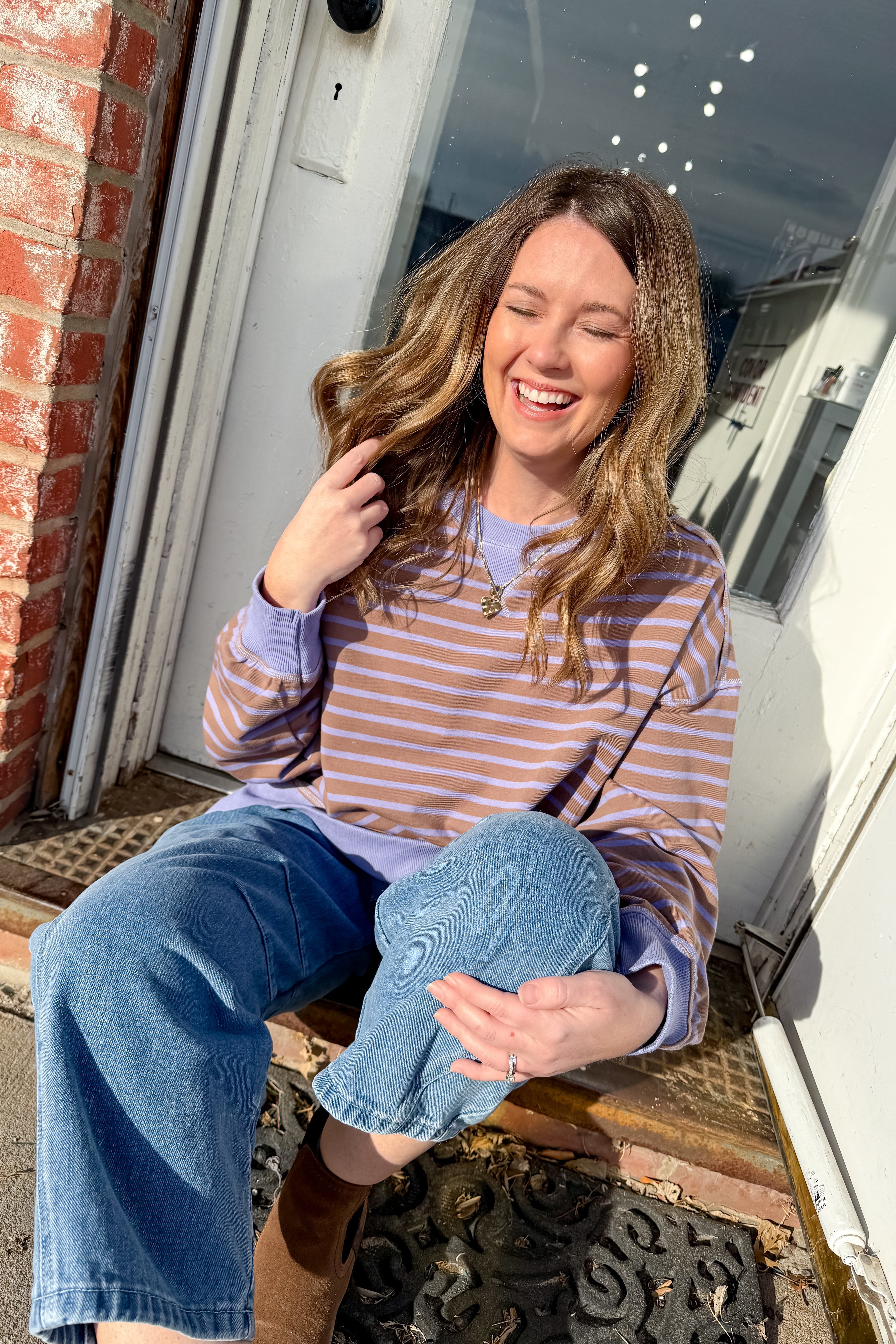 Woman sitting on a step outside, wearing a striped shirt and jeans.